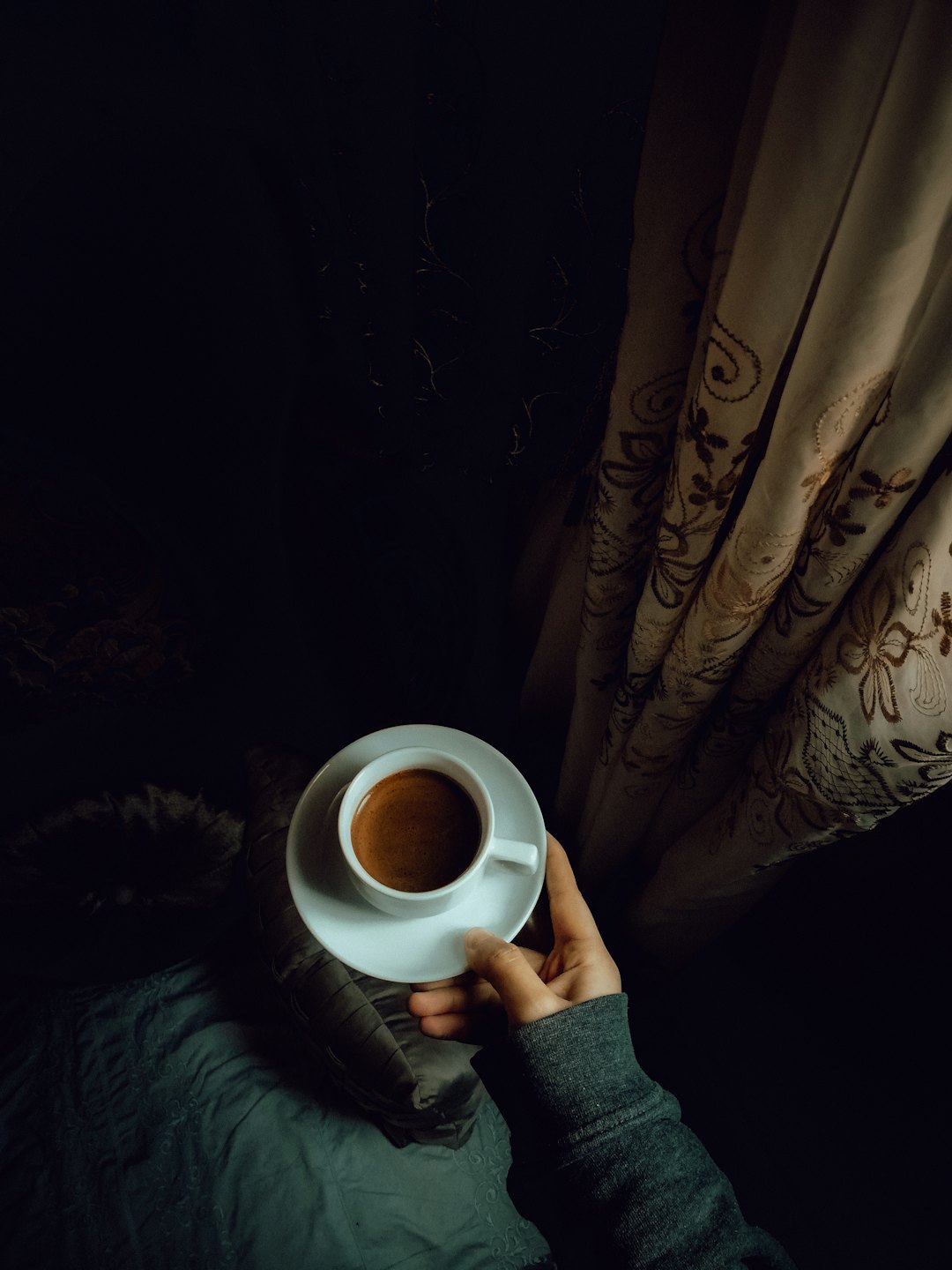 Hand in a grey sweater holds a coffee cup.