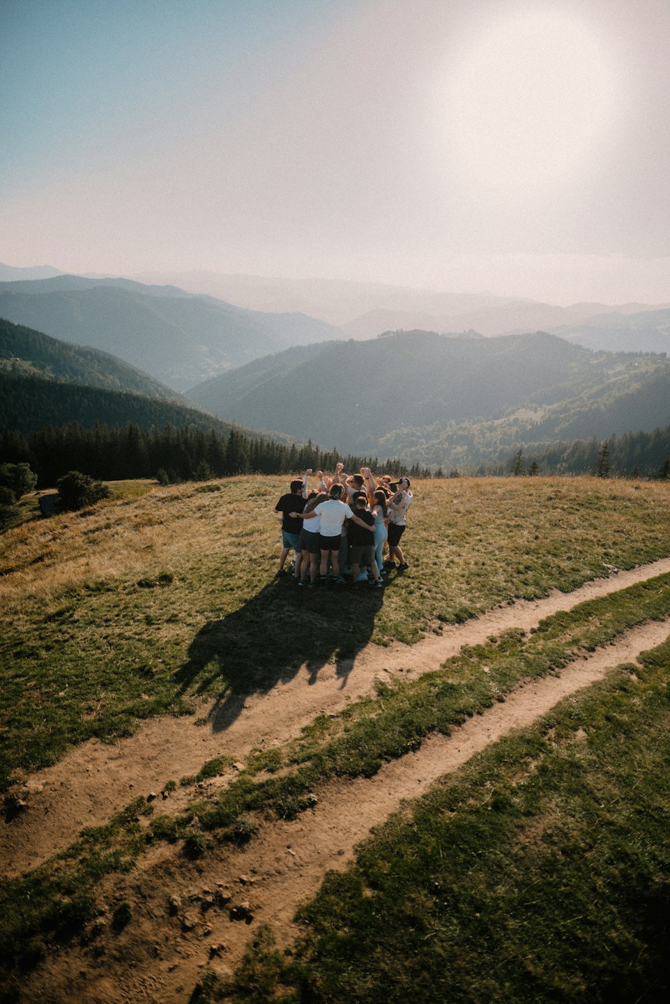 Friends huddle together on a grassy mountain hilltop.