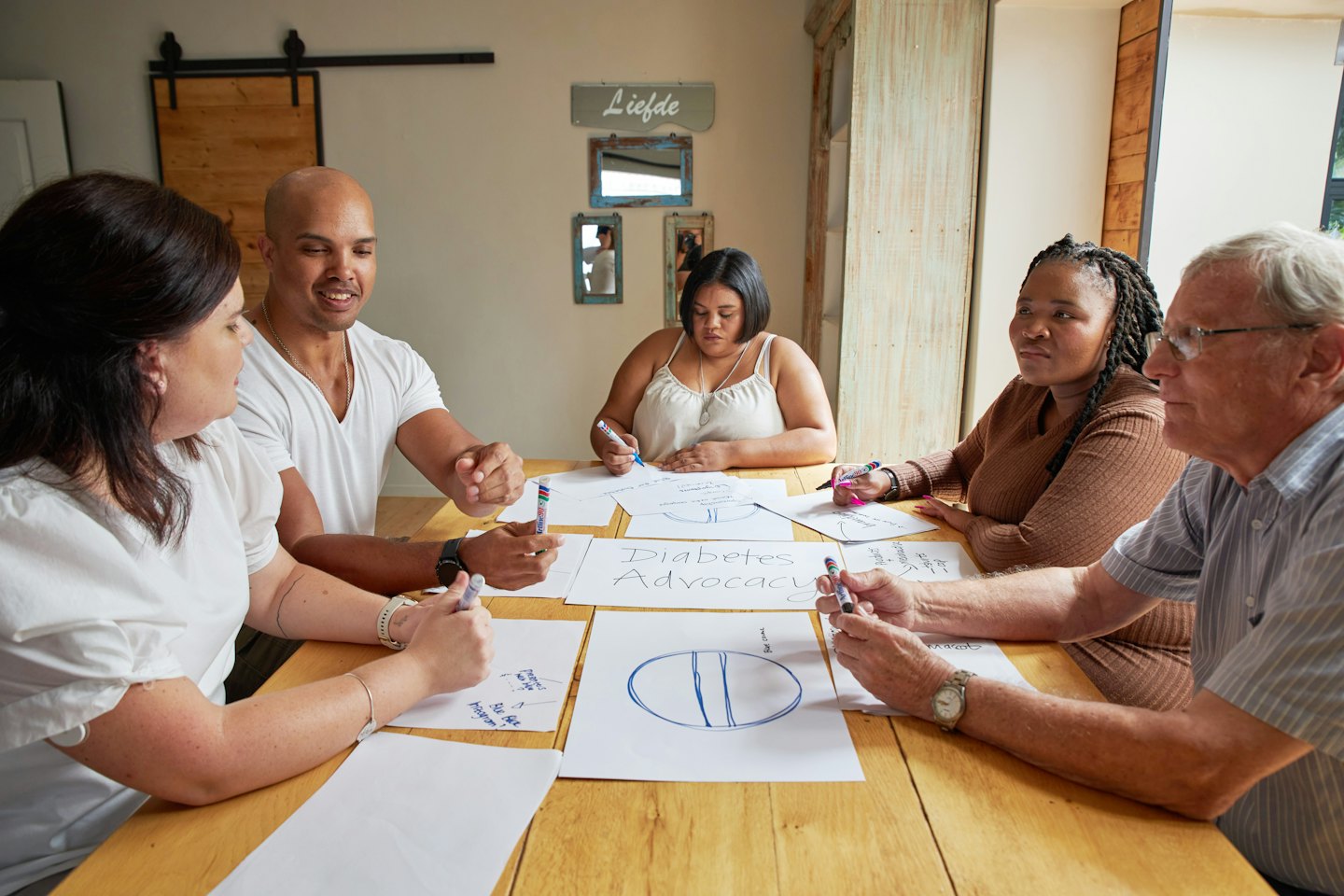 Diverse adults collaborating around a table with 'Diabetes Advocacy' papers.