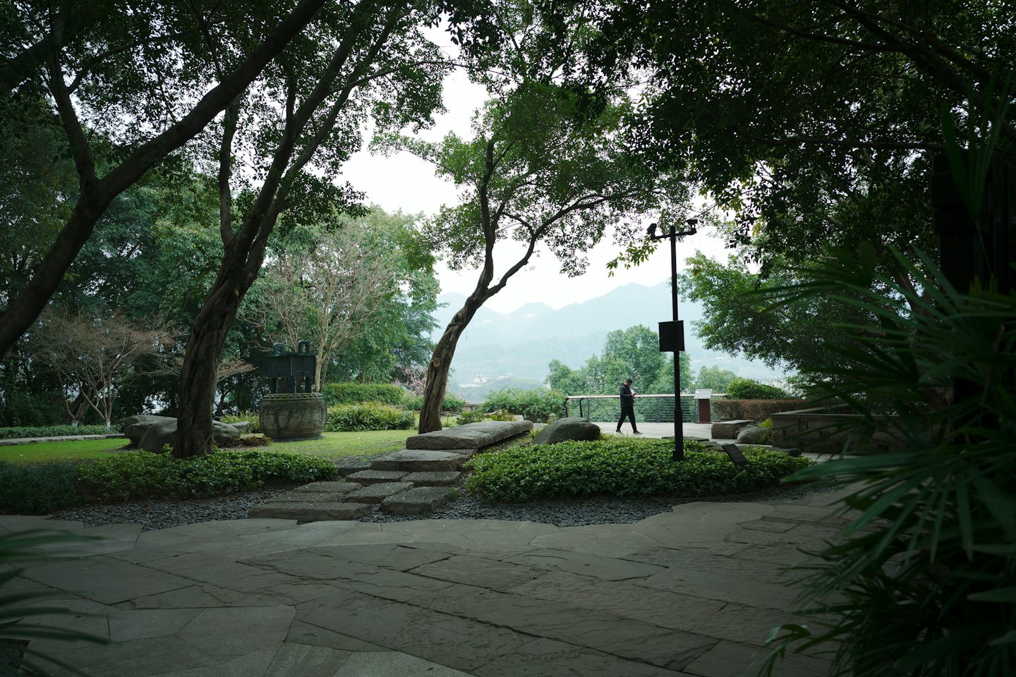 A lone person walks along a stone path in a garden.