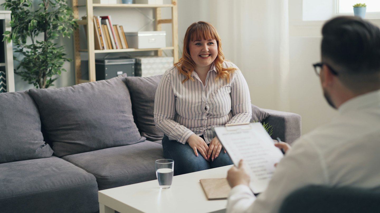 Woman with red hair smiles during a consultation on a sofa.